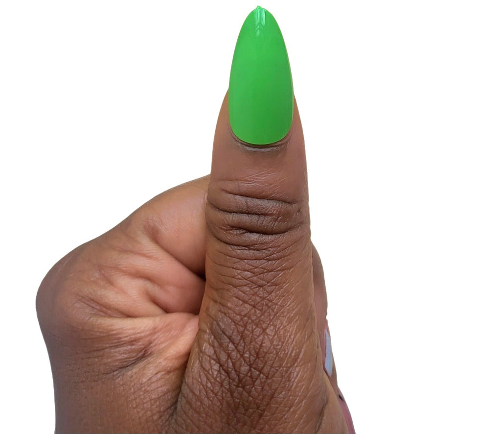 A hand model giving a thumbs up while showcasing a single glossy almond fake nail in a vibrant clover green shade from the Essentials Press-On Kit by Bloom Gloss Co.