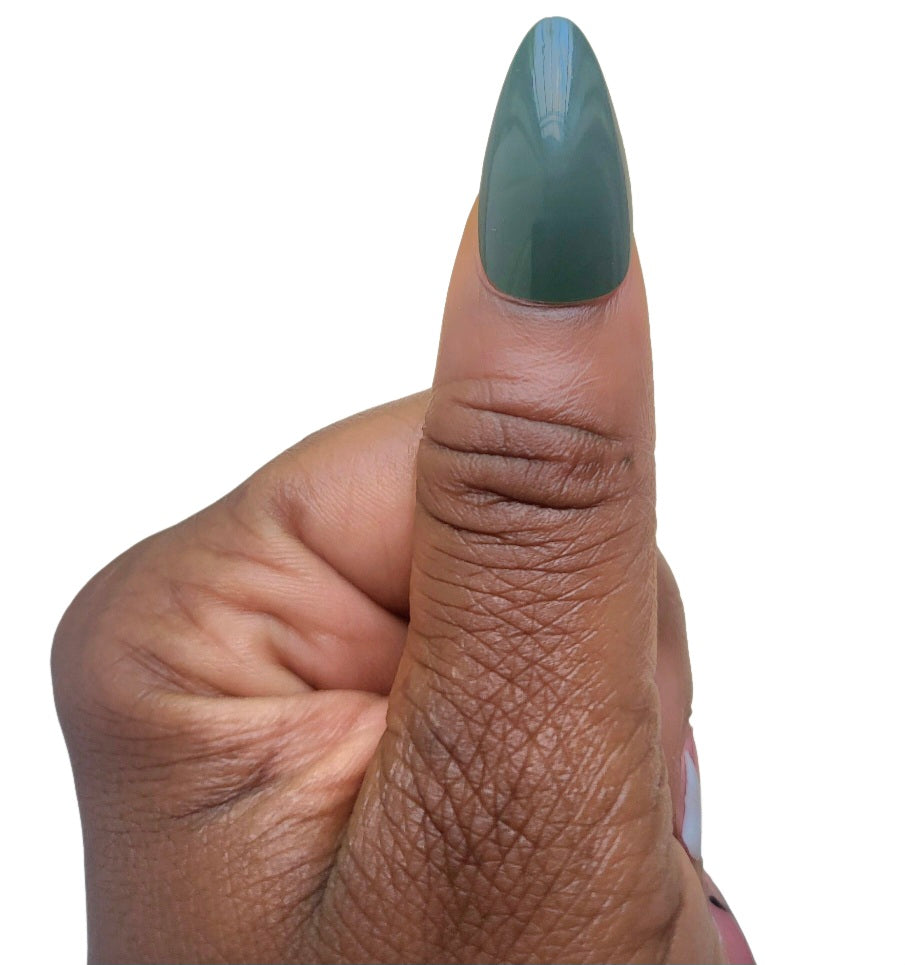 A hand model giving a thumbs up while showcasing a single glossy almond fake nail in an ivy jade green shade from the Essentials Press-On Kit by Bloom Gloss Co.