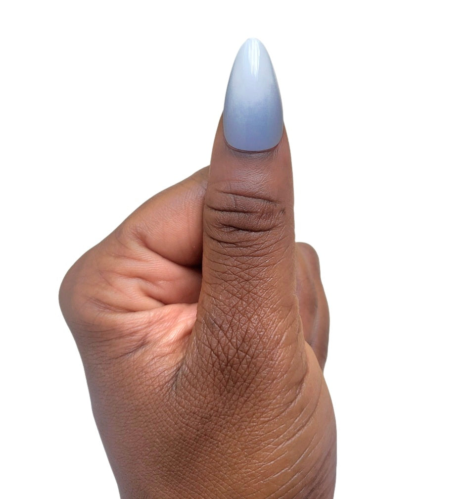 A hand model giving a thumbs up while showcasing a single glossy almond fake nail in a semi-translucent milky white shade from the Essentials Press-On Kit by Bloom Gloss Co.