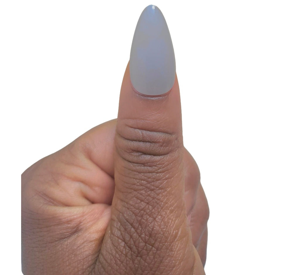 A hand model giving a thumbs up while showcasing a single matte almond fake nail in a light olive green shade from the Essentials Press-On Kit by Bloom Gloss Co.