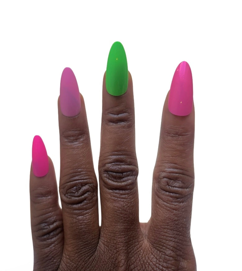 A hand model showcasing the Essentials Press-On Kit by Bloom Gloss Co, wearing glossy almond-shaped fake nails in a mix of vibrant pretty pop magenta, bubblegum pink, and clover green colors.