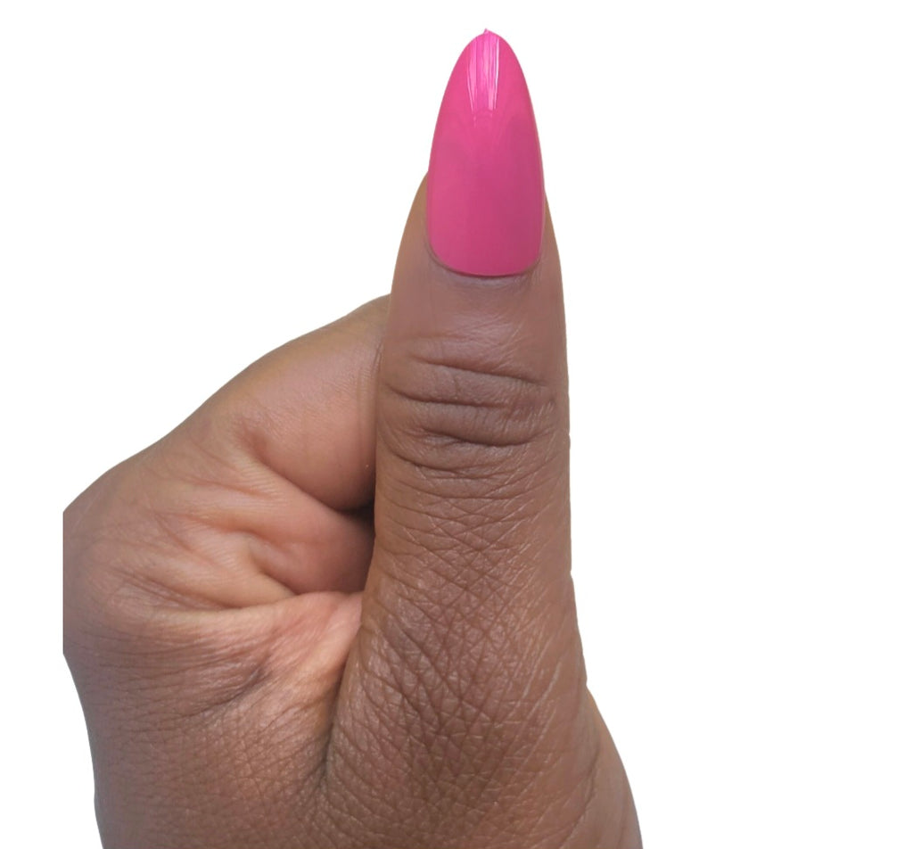 A hand model giving a thumbs up while showcasing a single glossy almond fake nail in a vivid pretty pop magenta shade from the Essentials Press-On Kit by Bloom Gloss Co.