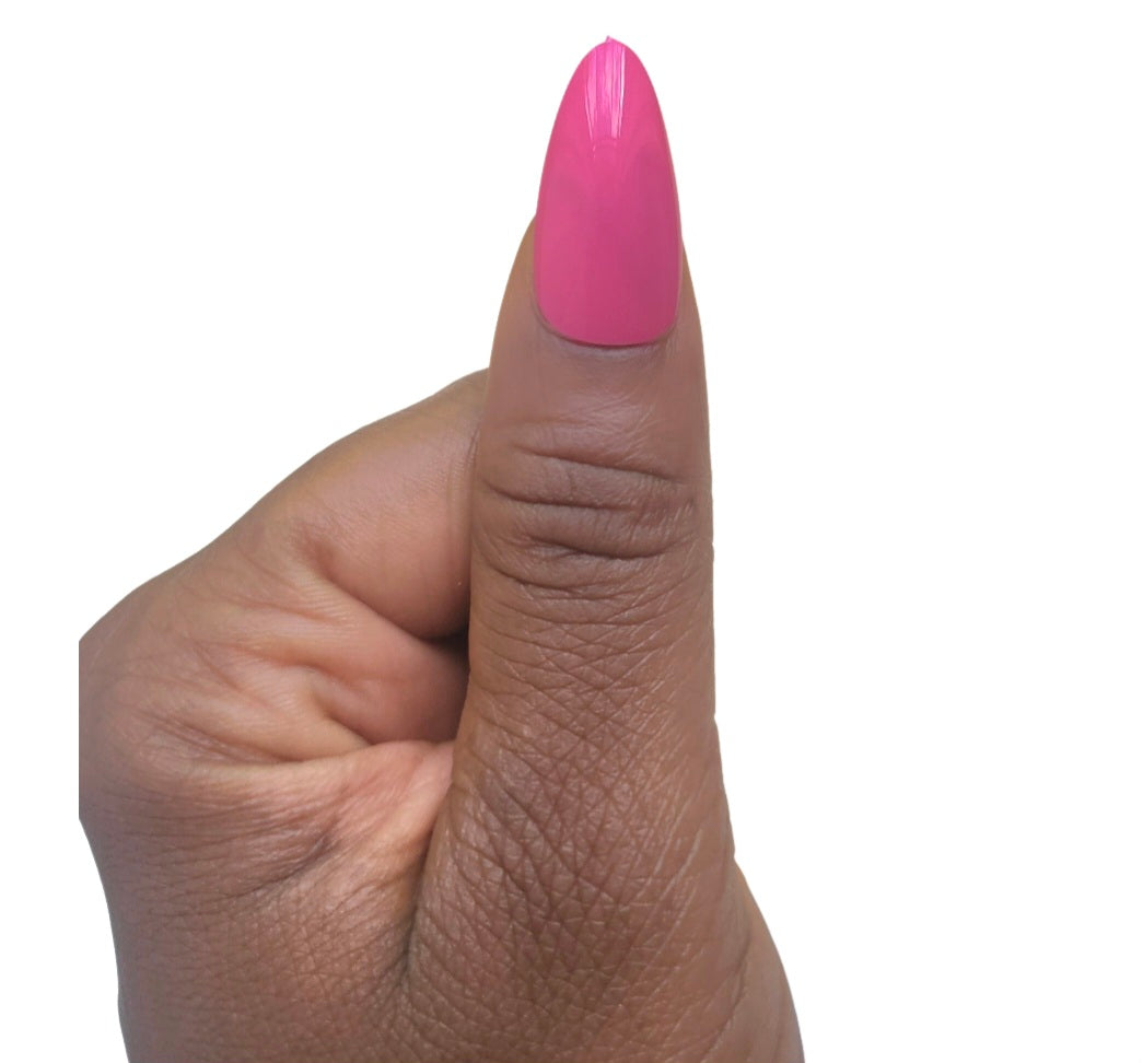 A hand model giving a thumbs up while showcasing a single glossy almond fake nail in a vivid pretty pop magenta shade from the Essentials Press-On Kit by Bloom Gloss Co.